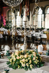 Decorated tables for guests at the wedding, there are candlestick, wine glasses, plates, napkins, tablecloth, fresh flowers