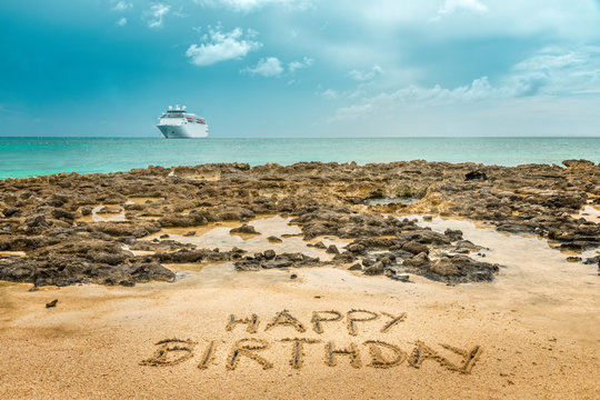 Handwritten  "Happy Birthday" on the sandy beach by the ocean with a cruise ship in the background