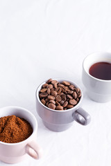 Three cups of different condition of coffee - beans, freshly ground and coffee drink on a marble light grey background.