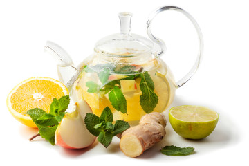 isolated glass transparent teapot with tea from ginger root, lime, orange, apple, mint on a white background