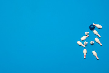 Knocked over bowling pins surrounding a bowling ball after rolling a strike on a blue background with copy space and room for text with a right side composition.
