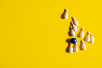 Bowling ball surrounded by knocked over bowling pins after rolling a strike on a yellow background with copy space and room for text with a right side composition. - obrazy, fototapety, plakaty