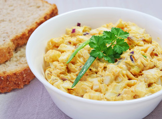 Homemade egg salad in white bowl with bread slices