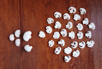 White mushrooms on an old wooden table are sliced and arranged. The process of cooking mushrooms is beautifully laid out at home on the table.