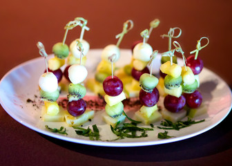 Bright canapes of grapes, kiwi, cheese, pineapple on a white plate in the restaurant at the event. Wooden skewers are beautifully decorated with amazing delicious canapés