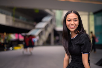 Happy young beautiful Asian tourist woman at the mall outdoors