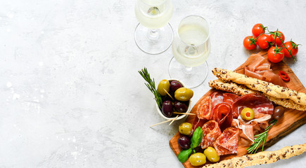 Traditional Italian appetizers ( antipasto ) : salami, bresaola, prosciutto, olives. Aperitif in Italy in Florence, Rome, aperitif in Milan. Two glasses of Prosecco and sticks of cereal bread - obrazy, fototapety, plakaty