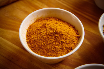 Turmeric powder in white bowl on wooden background