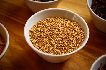 Yellow mustard seeds in white bowl on wooden background