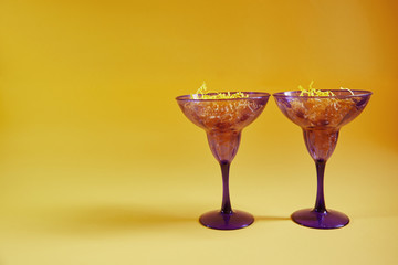 Two purple glasses stand on a table with a yellow background. In a glass of paper drink.