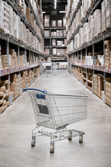 Empty shopping cart in a furniture store warehouse. Supermarket shopping basket aisle with box shelf abstract blur defocused background