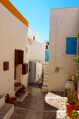 Fototapeta na wymiar One of the charms of Mykonos, Greek island in the heart of the cyclades, are its narrow streets : white houses with small flowered balconies touching almost above paved streets