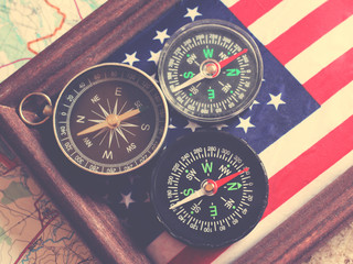 Three compasses and an American flag in a wooden frame, travel theme, top view