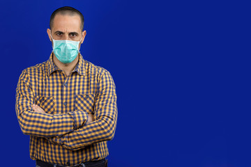 Uomo con camicia indossa una mascherina verde e incrocia le braccia , isolato su sfondo blu