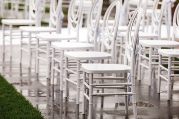 Fototapeta na wymiar Rows of white empty wet chairs outdoors before a wedding ceremony. selective focus