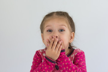 Portrait of funny caucasian child of three years old putting her hands on mouth to keep a silence and not to laugh in a loud looking at camera on the white background