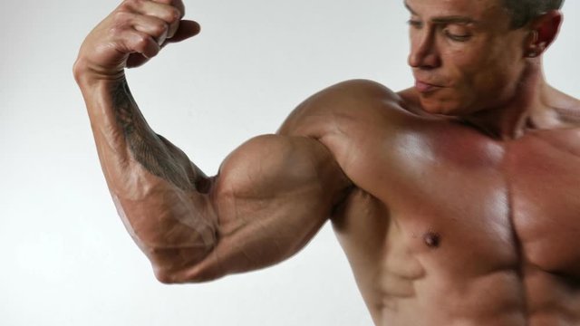 Muscular bodybuilder man standing, shirtless, showing chiselled torso, abs and pecs on white background in studio shot
