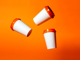 Three white paper cups with red lids hang in the air on an orange background.