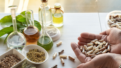 Female hands hold dietary supplement capsules near ingredients to create them