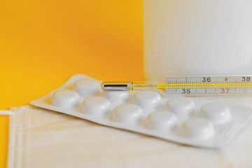 Fototapeta premium Medical disposable mask, pills and a mercury thermometer on a yellow background. Copy, empty space for text
