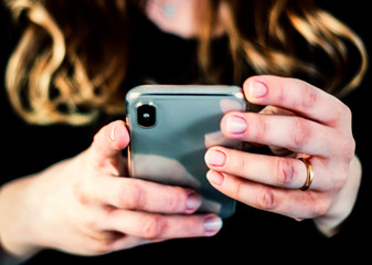 the hands of a young caucasian brunette woman while holding a smartphone typing on the touch screen.