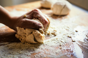 female hand kneading a flour dough by rolling it on a wooden board