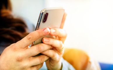 the hands of a young caucasian brunette woman while holding a smartphone typing on the touch screen.