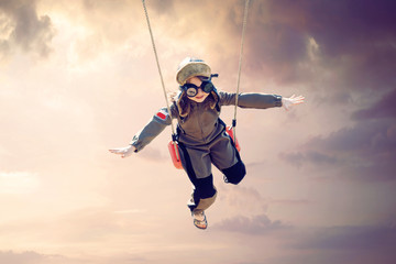 happy child girl wearing an aviator outfit swinging and flying deep in a sunset sky - positive...