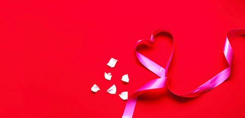 Festive pink ribbon in the shape of heart on red background with white rose petals. Mothers Day concept. Template mock up of greeting card or text design.