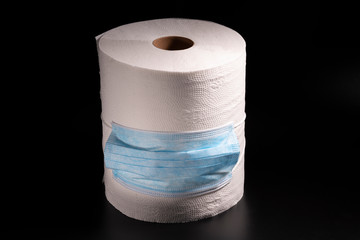 A large roll of toilet paper or paper towels with a medical mask on a black background