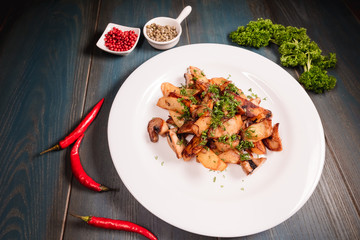 A plate of appetizing potato with mushrooms on a wooden table, among seasonings. Studio photography of food in the cooking industry, dark background.