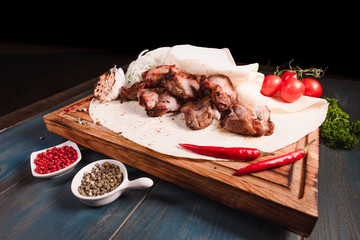 Appetizing fried meat lies on a wooden tray, among the seasonings. Studio photography of food in the cooking industry, dark background