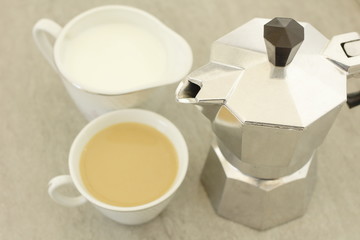 cafetera metálica junto a una taza de café y  una jarra de leche pequeña, leche, cafeína,...