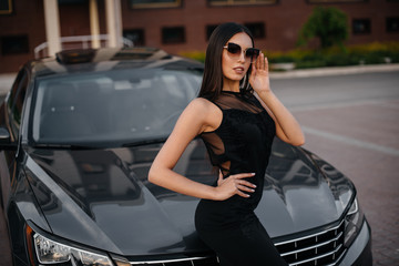 Stylish young girl stands near the car in a black dress. Business fashion and style