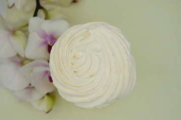 Meringues. Protein sugar cake  and branch of white orchid on yellow background. Copy space.