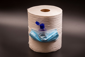 A large roll of toilet paper or paper towels, hand antiseptic with a medical mask on a black background