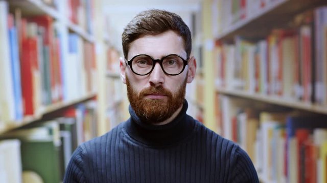 Indoor portrait bearded young man librarian or student wearing glasses keeping order in the library. Isolated on background. People and education concept.