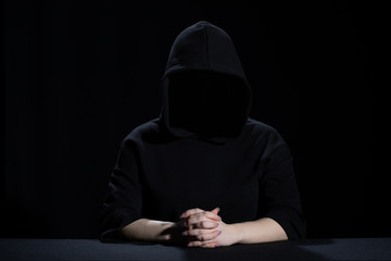 A faceless woman emerges from the dark dressed in black.