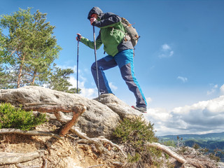 Man with long legs, running shoes on feets climbing up rocky hillside