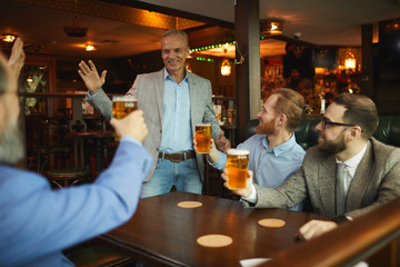 Group of businessmen greeting their colleague while sitting in cafe and drinking beer after work
