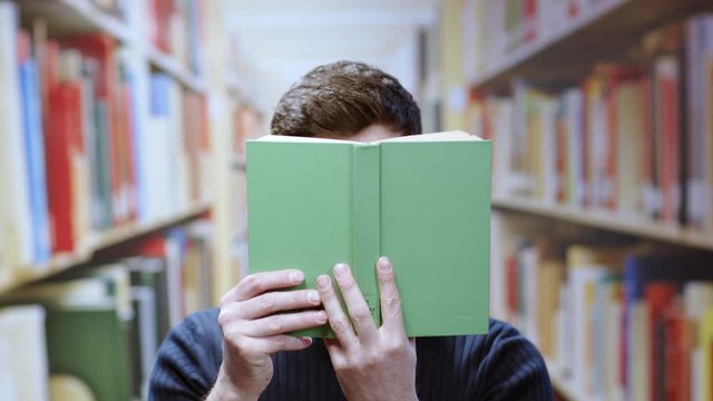 Real portrait of scared young hipster reading a college book literarture spying people around hide playing fun comedy in the library.