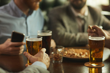 Close-up of friends sitting at the table with glasses of beer and spending a funny time in the pub