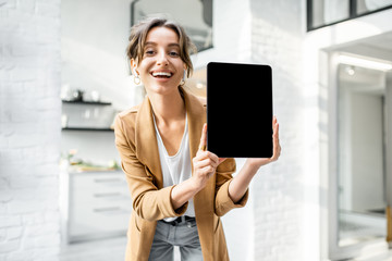 Well-dressed cheerful business woman with a digital tablet indoors, showing tablet with a black...