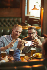 Two friends posing at camera on mobile phone while resting in the bar with alcohol drinks