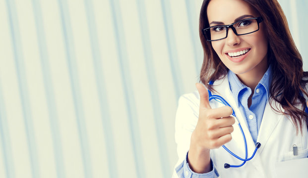 Happy smiling female doctor in glasses, showing thumbs up hand sign gesture, at office, with blank copyspace area for slogan or text. Online concultation and healthcare concept picture.