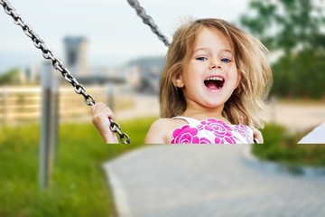 Little child blond girl having fun on a swing