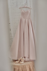 pink wedding dress on a hanger with shoes nearby