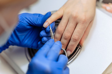 Fototapeta na wymiar Closeup process of professional Female manicure master at beauty salon removes dry cuticle skin near nails cutting it with scissors. Concept of body care. Beautician file nails to a customer