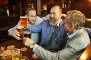 Senior bearded man toasting with glass of beer together with his workers they celebrating successful deal in the pub