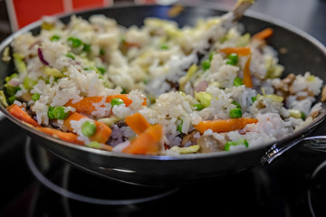 Close up and selective focus on egg rice, carrot, mushroom and green pea dish cooking in a non-stick wok on the hob